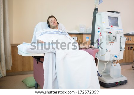 Young male patient sleeping while listening to music during renal dialysis treatment in hospital room