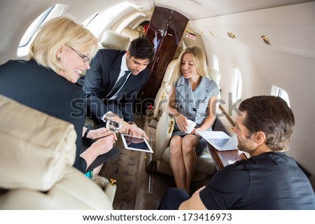Businessman showing presentation on digital tablet with colleagues in corporate jet
