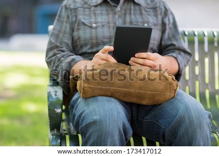 Midsection of male university student using digital tablet on bench at campus