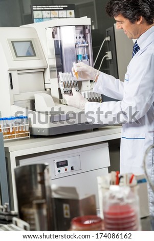 Male scientist using urine analyzer to test samples in medical lab