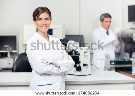 Portrait of confident female scientist with colleague in background at laboratory