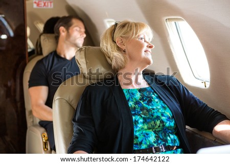 Happy mature businesswoman with man sleeping behind on private jet