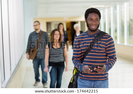 Young male university student with digital tablet standing on university corridor