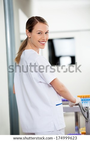 Portrait of happy female lab technician pushing medical cart in corridor