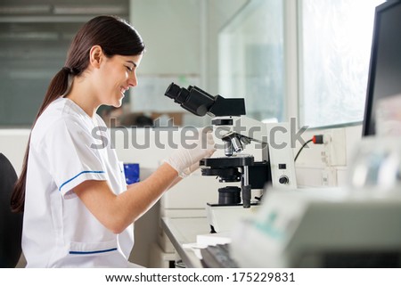 Happy young female scientist using microscope in laboratory