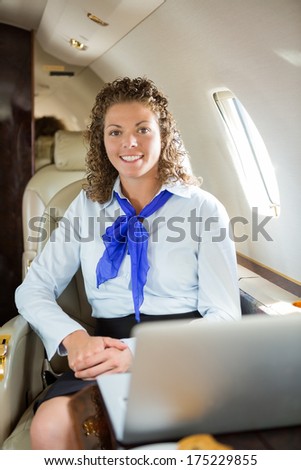 Portrait of happy airhostess with laptop sitting in private jet