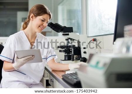Happy young female researcher holding digital tablet in medical laboratory
