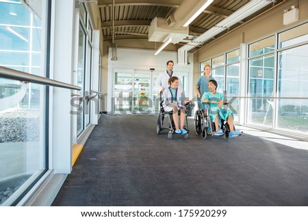 Doctor and nurse pushing patients on wheelchairs at corridor in hospital