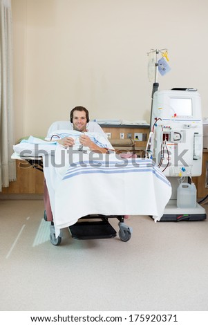 Portrait of smiling male patient listening music while receiving renal dialysis treatment in hospital room