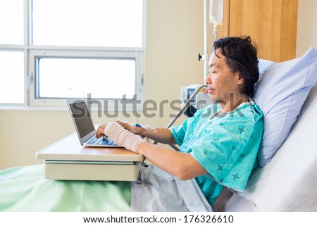 Side view of mature male patient using laptop on bed in hospital