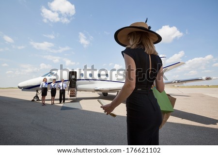Rear view of woman walking towards pilot and stewardesses against private jet at airport terminal