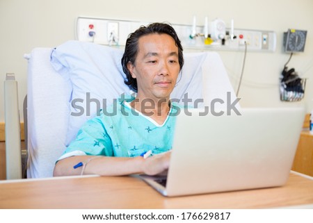 Mature male patient using laptop on bed in hospital