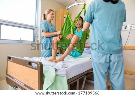 Male patient sitting on hydraulic lift while looking at nurse in hospital