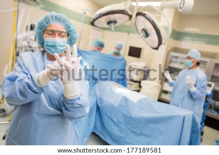Mature female surgeon in operating suite adjusting latex gloves