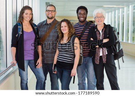 Group portrait of confident multiethnic university students standing in corridor with professor