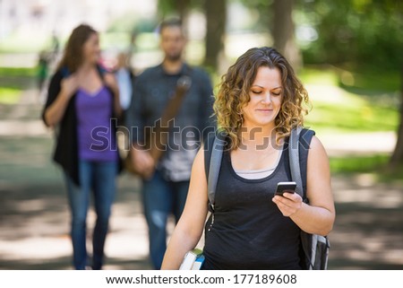 Mid adult female student with backpack using cellphone while standing on campus