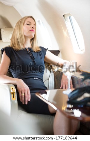 Beautiful rich woman with eyes closed relaxing in private jet
