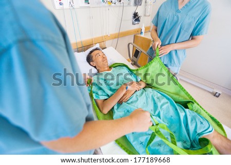 Midsection of nurses preparing mature patient before transferring him on hydraulic lift at hospital