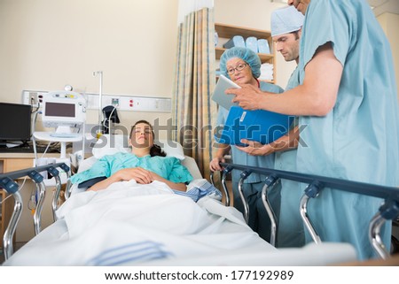 Multiethnic nurses discussing female patient\'s report by bed in hospital ward