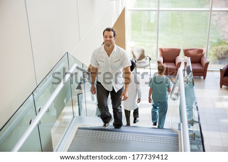 Full length male patient and medical team walking on stairs in hospital