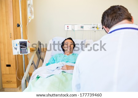 Smiling male patient looking at doctor while lying on bed in hospital room