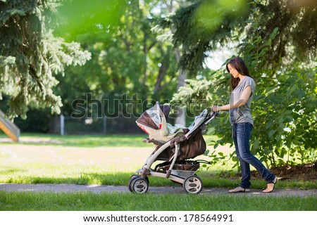 Full length of young mother pushing a stroller in the park Full length of young mother pushing a stroller in the park