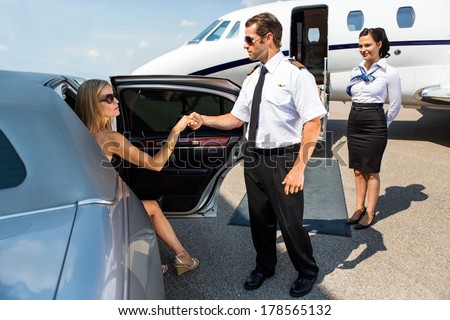 Full length of pilot helping elegant woman stepping out of car at airport terminal