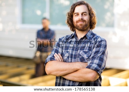 Portrait of confident mid adult carpenter with arms crossed at construction site