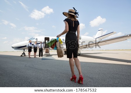 Full length rear view of woman carrying shopping bags while walking towards private jet at airport terminal
