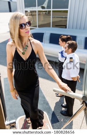 Full length of rich woman boarding private jet with pilot and airhostess standing by at airport terminal