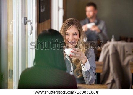 Beautiful young woman with female friend having coffee at cafe