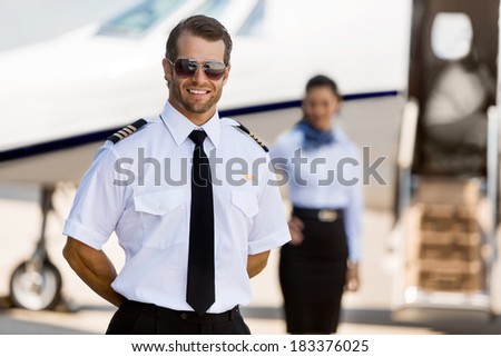 Portrait of confident pilot standing with stewardess and private jet in background at terminal