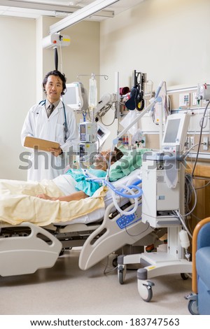 Portrait of male doctor with patient\'s report standing by bed in hospital room