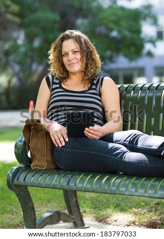 Portrait of confident university student with digital tablet sitting on bench at campus