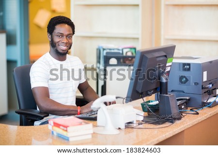 Portrait of confident male librarian working at desk in library