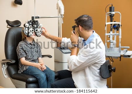 Mid adult male optometrist examining preadolescent boy\'s eyes in clinic