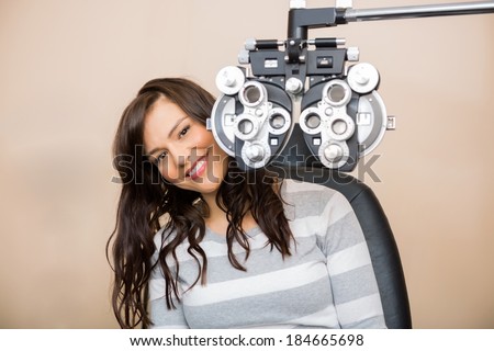 Portrait of happy young woman sitting behind phoropter during eye exam