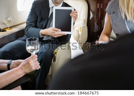 Cropped image of businessman showing digital tablet to colleagues in private jet