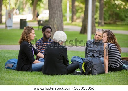 Group of multiethnic friends relaxing on grass at university campus during outdoor class