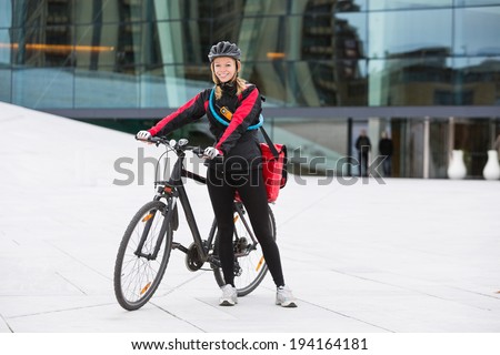 Portrait of young female cyclist in protective gear with courier delivery bag