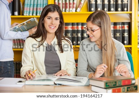 Portrait of happy female student with friend sitting at table in university library