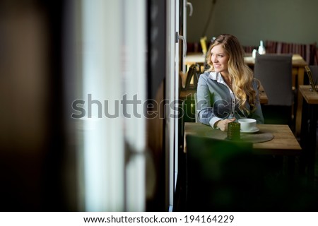 Attractive young woman sitting alone in cafe looking out window