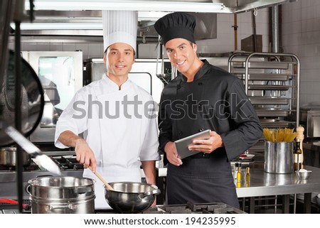 Portrait of happy chefs with digital tablet cooking food in commercial kitchen