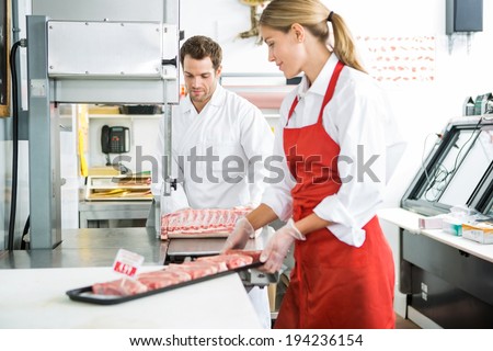 Male and female butchers processing meat in store