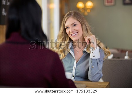 Happy young woman with friend having coffee at cafe