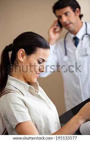 Side view of pretty young female working while doctor on a phone call in background