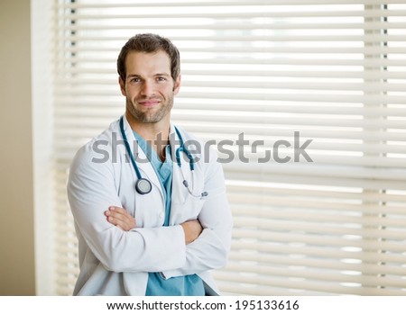 Portrait of confident young male doctor standing arms crossed at clinic