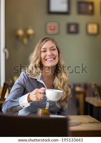 Portrait of happy young woman drinking coffee at coffeeshop