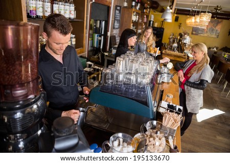 Male bartender working at counter while female colleague serving coffee to customer