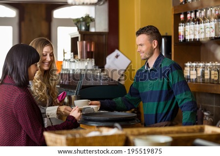 Handsome bartender serving coffee to women at counter in cafe